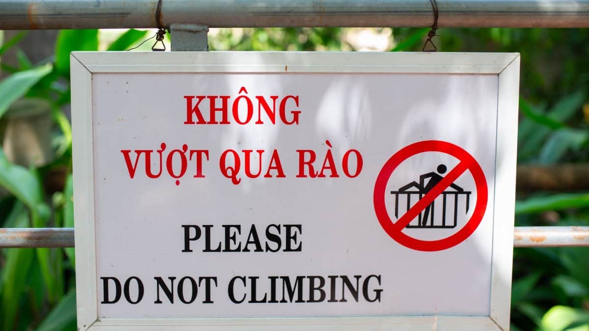 Bilingual safety sign warning against climbing, displayed outdoors with green foliage.