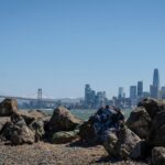 View of San Francisco skyline featuring the Bay Bridge and rocky coast under a clear blue sky.