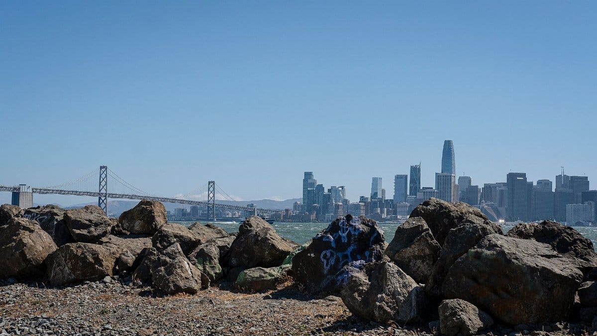 View of San Francisco skyline featuring the Bay Bridge and rocky coast under a clear blue sky.