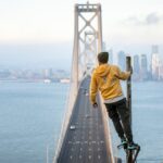 Person standing on a pole with a thrilling view of the San Francisco Bay Bridge and city skyline.
