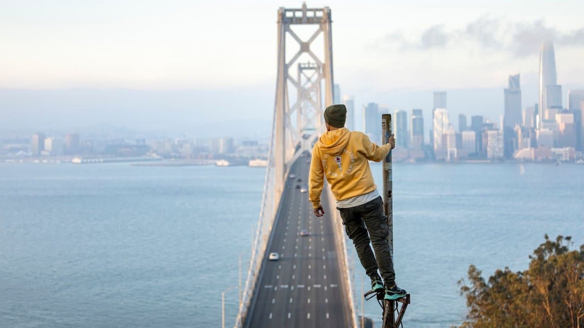 Person standing on a pole with a thrilling view of the San Francisco Bay Bridge and city skyline.