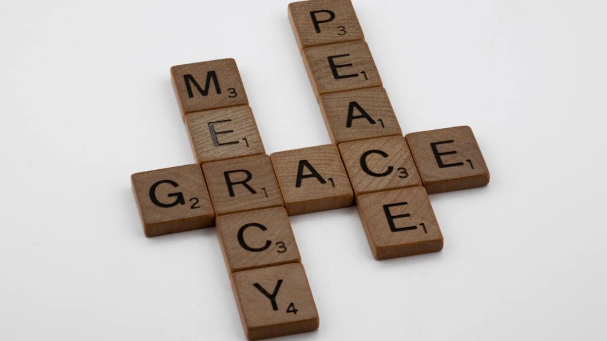 Wooden tiles spelling PEACE, MERCY, GRACE in crossword style on white background.