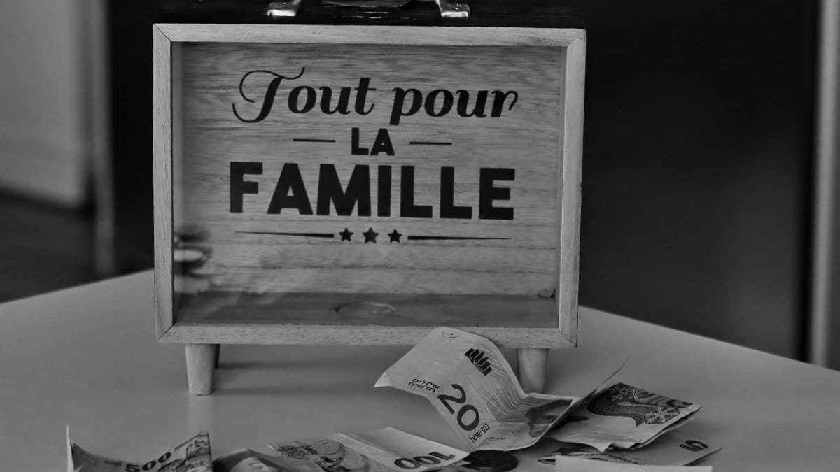 Black and white photo of a money box and various currencies on a table, symbolizing savings for family.