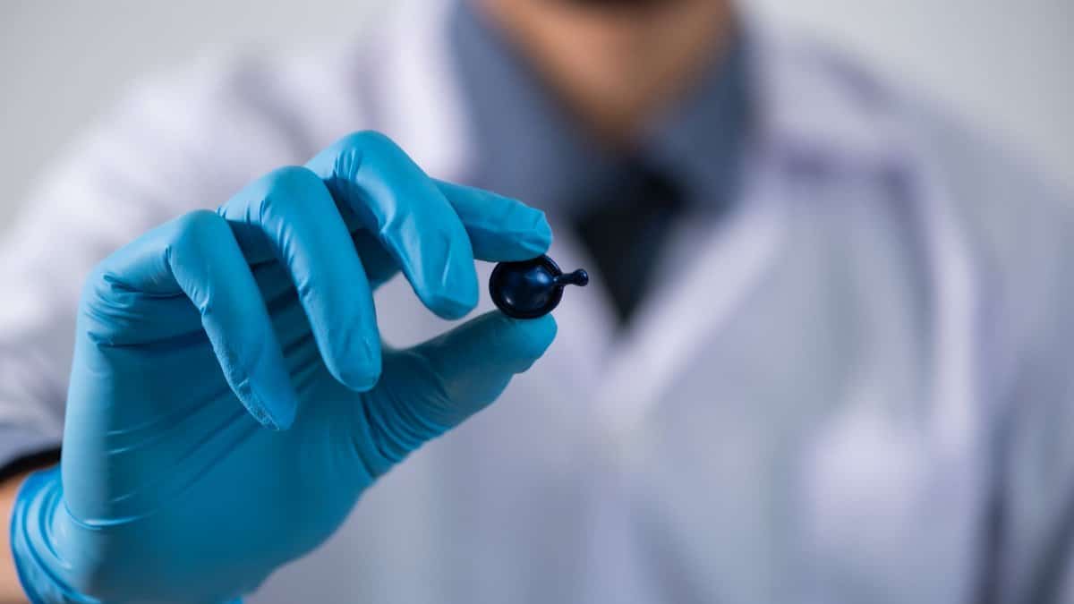 A scientist wearing gloves holding a small capsule in a laboratory setting, showcasing healthcare and research.