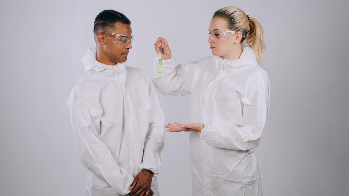 Two scientists wearing protective suits and goggles discussing a test tube experiment.