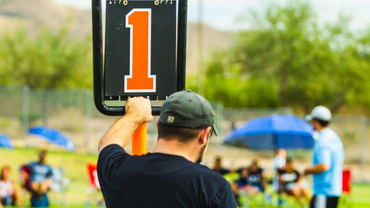 Back view of anonymous male trainer standing near scoreboard on blurred background of field during sports competition