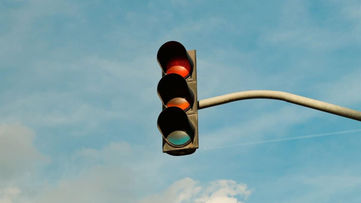A traffic light with red signal set against a blue sky, signifying stop in urban streets.