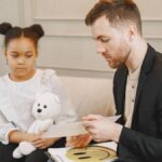 A child holding a plush toy listens to a man in a therapy session.