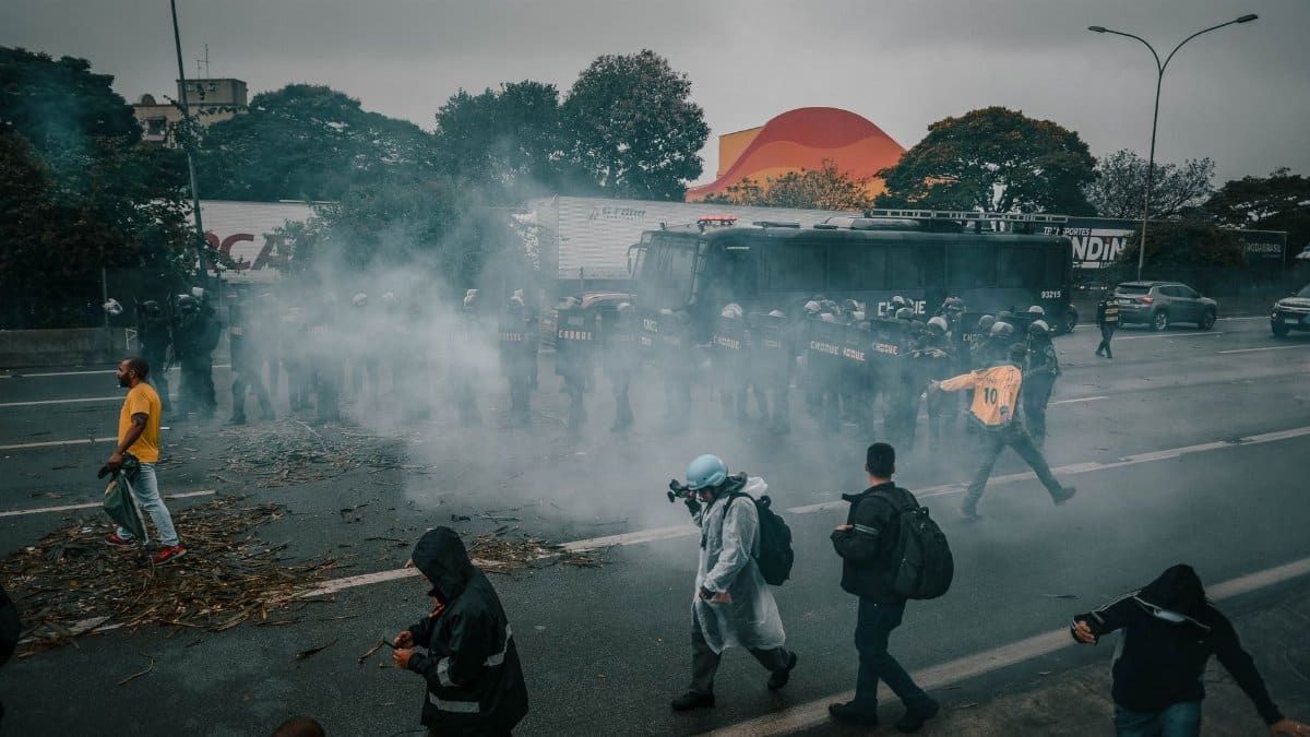 A tense urban protest scene with police and smoke surrounding demonstrators on the street.