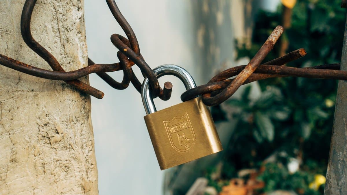 A brass padlock securing a rusty wire on a concrete post, symbolizing security and protection.