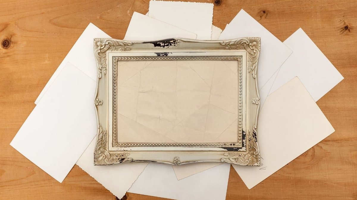 Rustic wooden surface with an ornate vintage frame surrounded by blank white papers, perfect for design mockups.