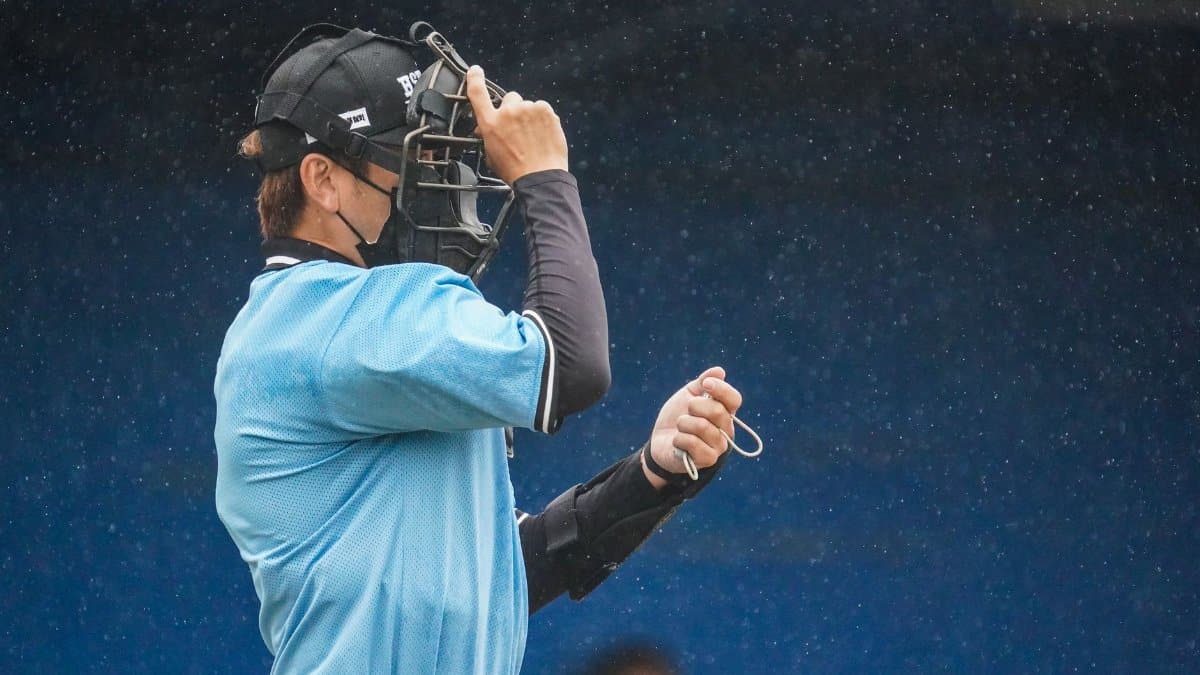 A baseball umpire adjusts his mask during a rainy sports event, capturing focus and dedication.