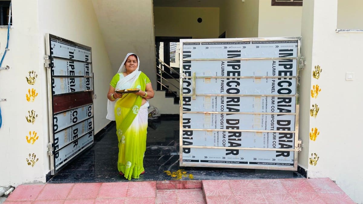 An Indian woman in a green and white sari stands at an entrance with a plate of offerings.