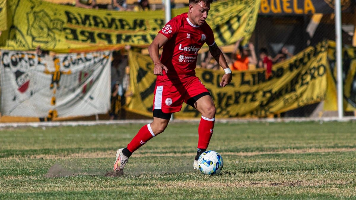 Soccer player in red kit dribbling the ball during a daytime match.