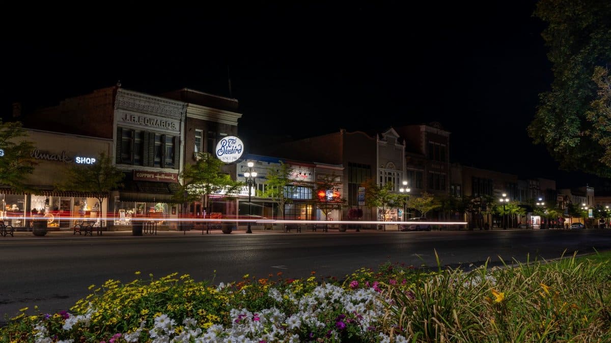 Captivating night scene of Logan, UT's historic downtown with light trails and blooming flowers.