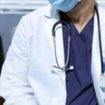 Close-up of a healthcare worker wearing a mask and stethoscope, seated indoors.