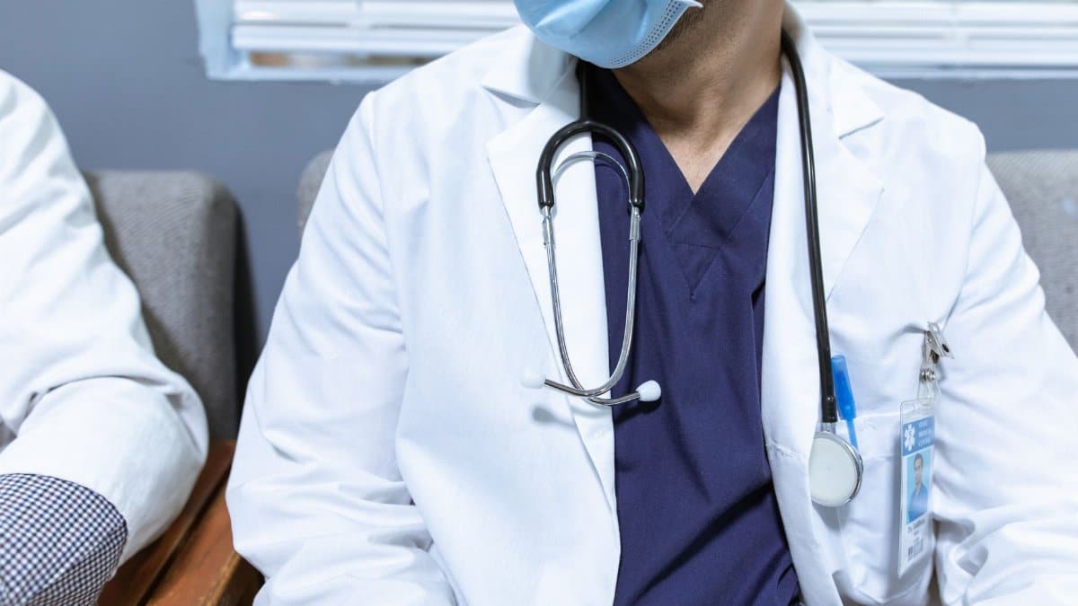 Close-up of a healthcare worker wearing a mask and stethoscope, seated indoors.
