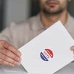 A man holds a voting envelope with a vote sticker. Symbolizes election participation.