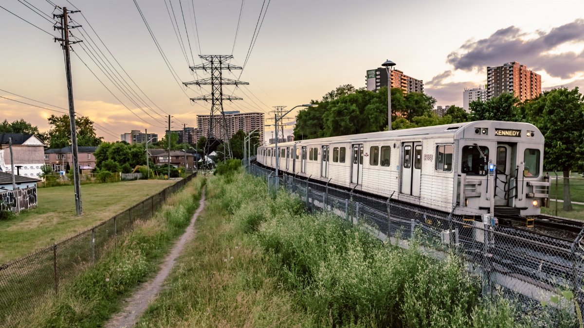 A Toronto subway train travels through a vibrant urban area at sunset, capturing the essence of the city.