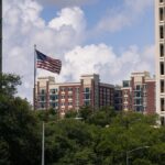 American flag waving between Houston skyscrapers on a sunny day.