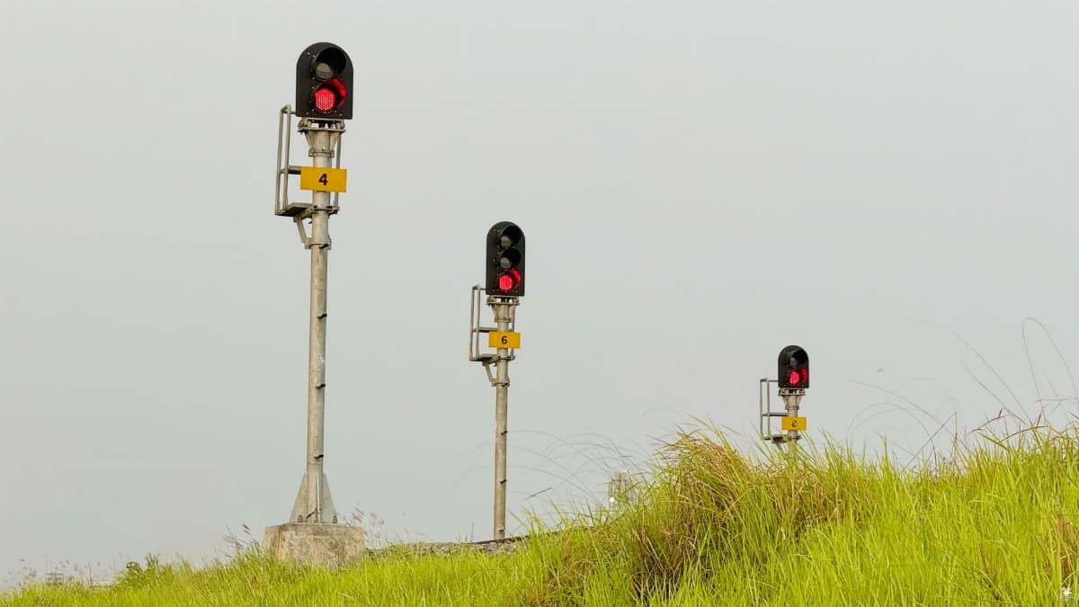 Three railway signals with red lights in a green grassy field under a clear sky.