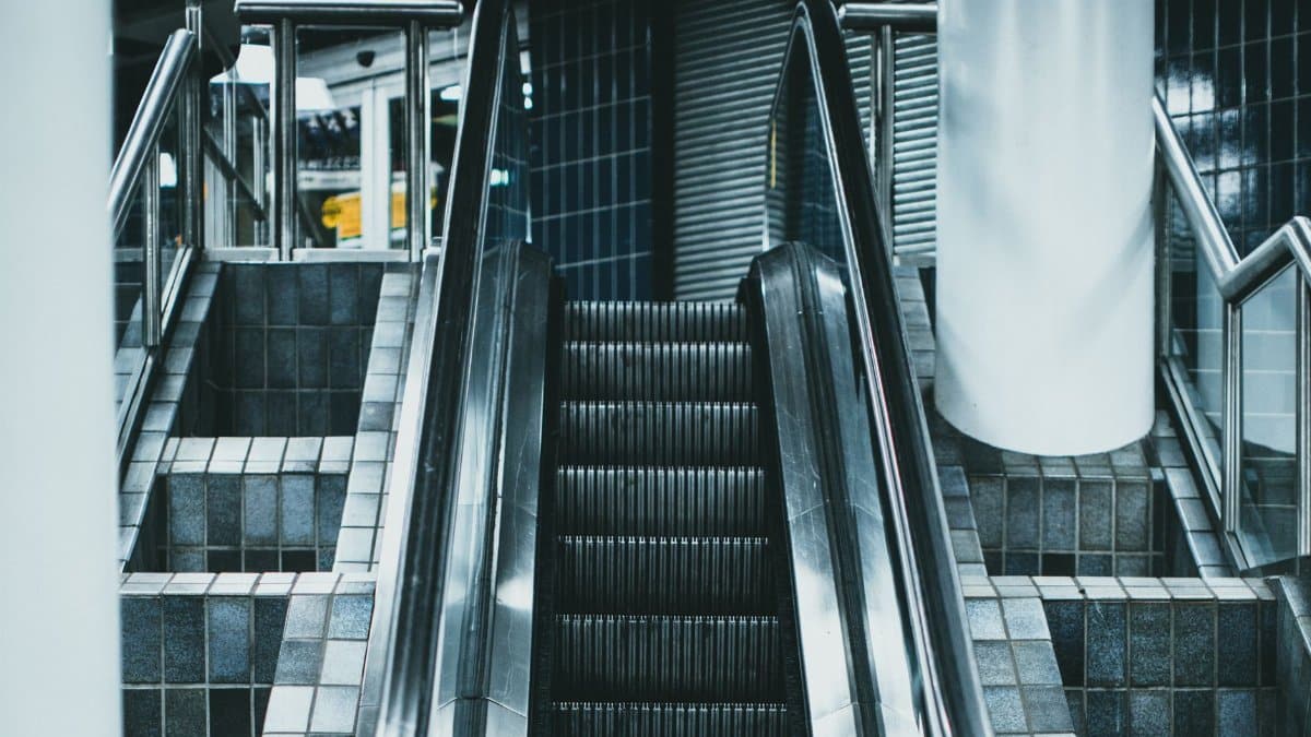 A modern subway escalator with stainless steel handrails and tiled steps in a dimly lit station.