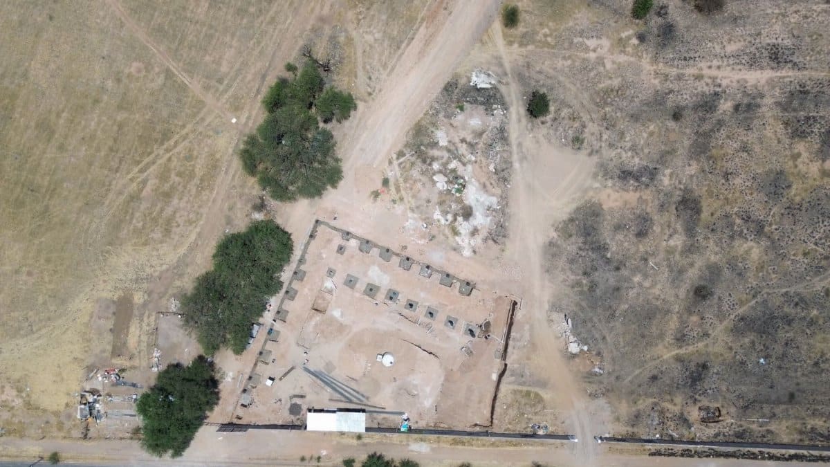 Aerial shot of a rural construction site with surrounding landscape and vehicles on a road.