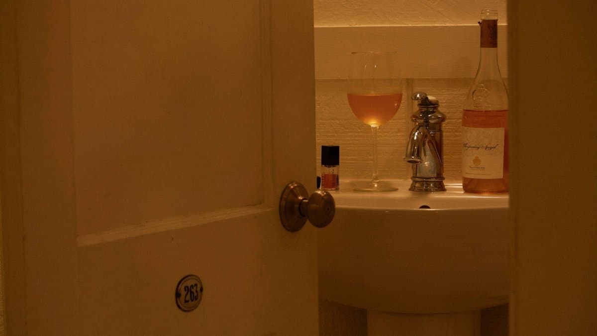 Warm lit bathroom with a rosé wine glass on sink, behind an open door.