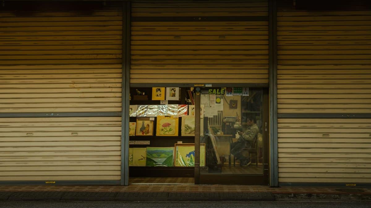 A cozy art studio displaying paintings through a window with a figure sitting inside.