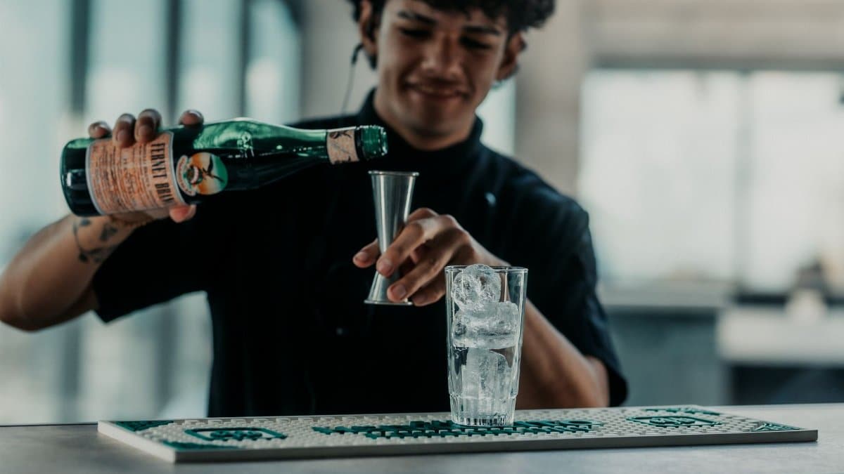 A bartender skillfully pouring Fernet into a glass in a modern Buenos Aires bar setting.
