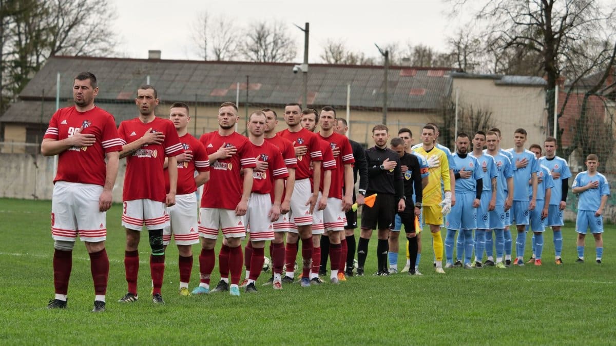 Two soccer teams stand in lines for a pre-match ceremony on a grass field.