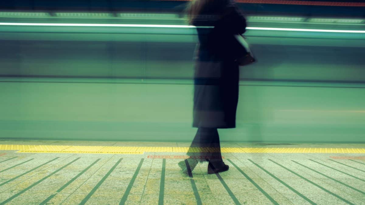 Woman waiting at Istanbul train station, blurred motion capturing a fast-moving train.