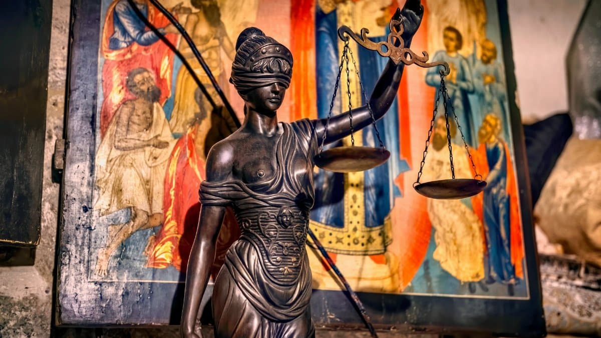 A blindfolded statue representing justice holding scales, set against an ornate background in Jerusalem.
