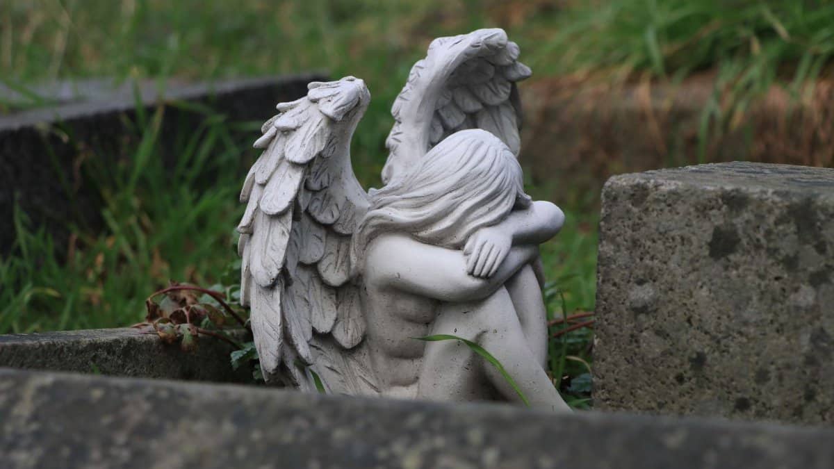 A tranquil angel statue resting in a lush, grassy cemetery conveying peace and serenity.