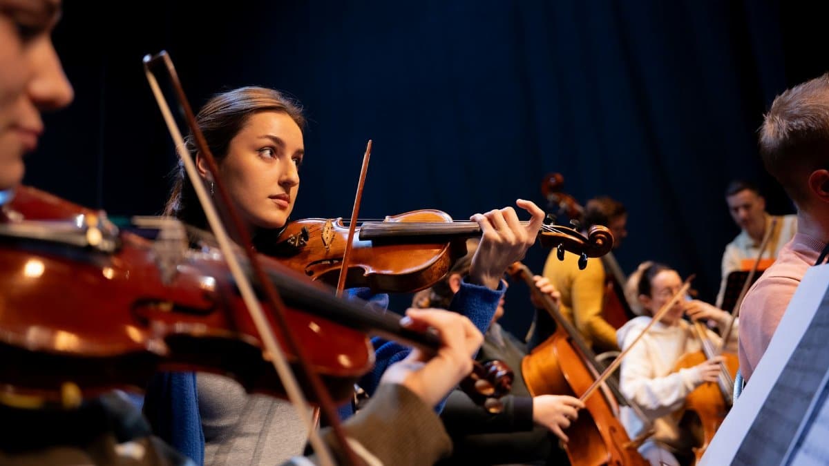 A group of musicians perform in an orchestra, featuring a violinist in focus.