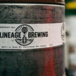 Close-up photo of a Lineage Brewing barrel with label details. Captured outdoors, offers an industrial feel.