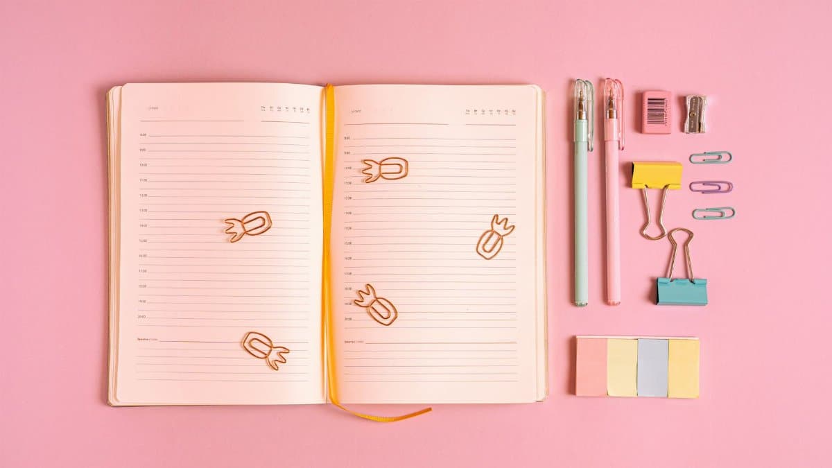 Flat lay of colorful office supplies with a notebook on a pink background. Ideal for workspace inspiration.