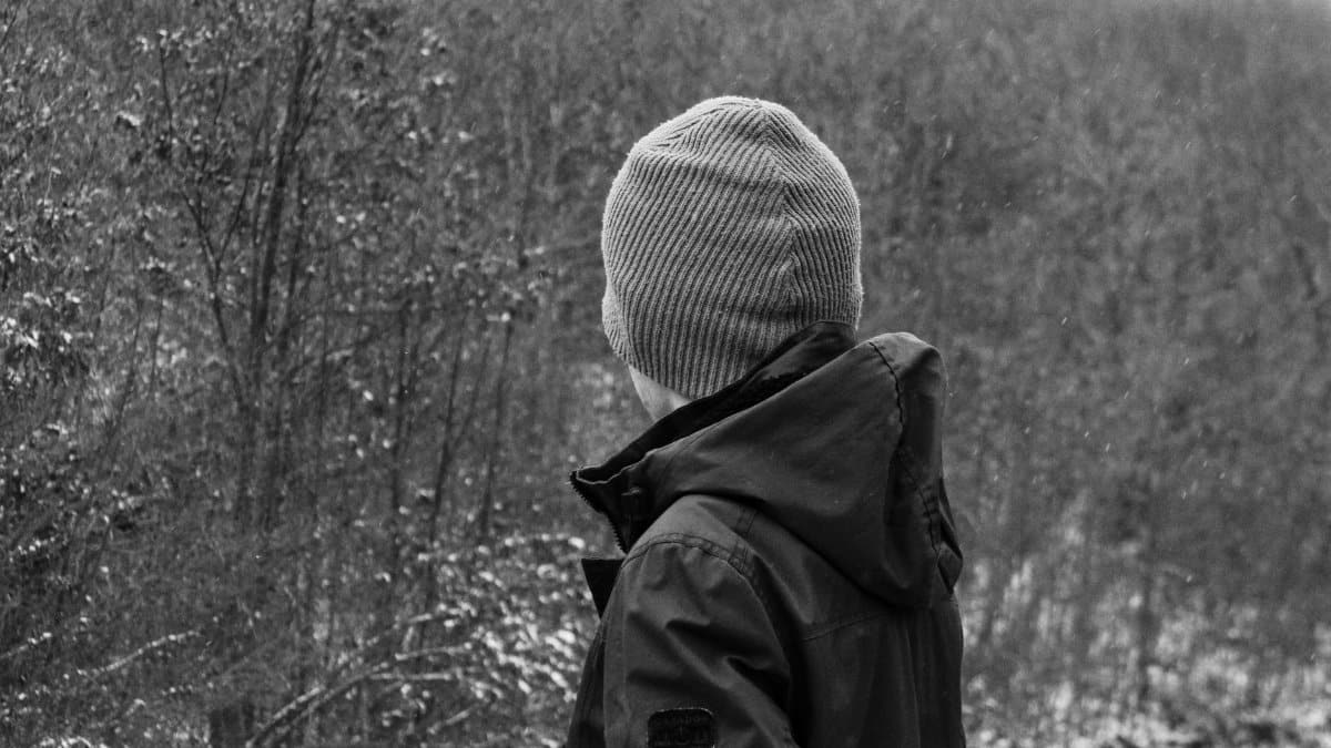 Back view of a person in winter attire standing in a snowy forest.