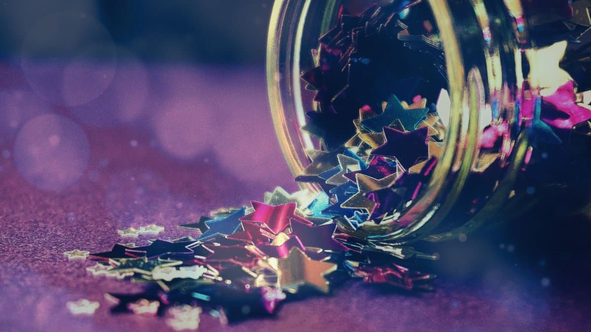 Colorful star-shaped confetti spilling out of a glass jar creates a festive and artistic scene.