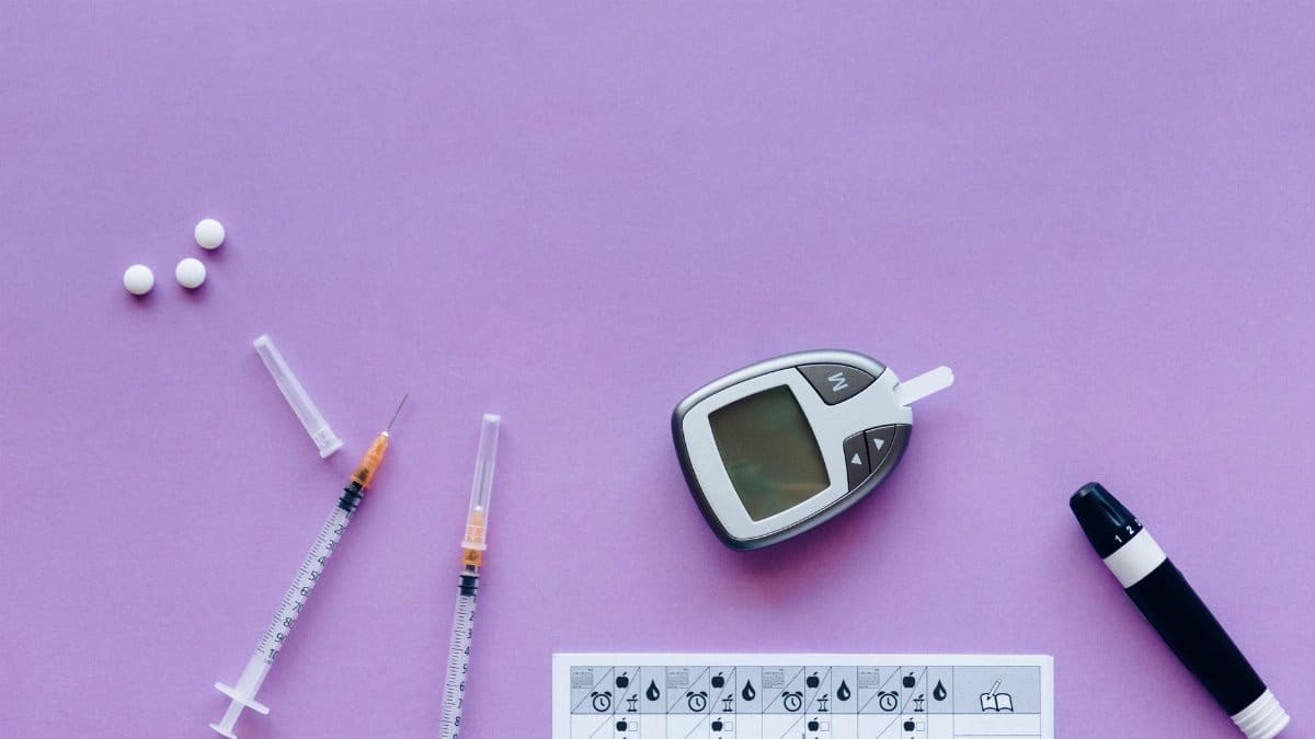 Flat lay of diabetes management tools including glucometer, syringes, and pills on purple background.