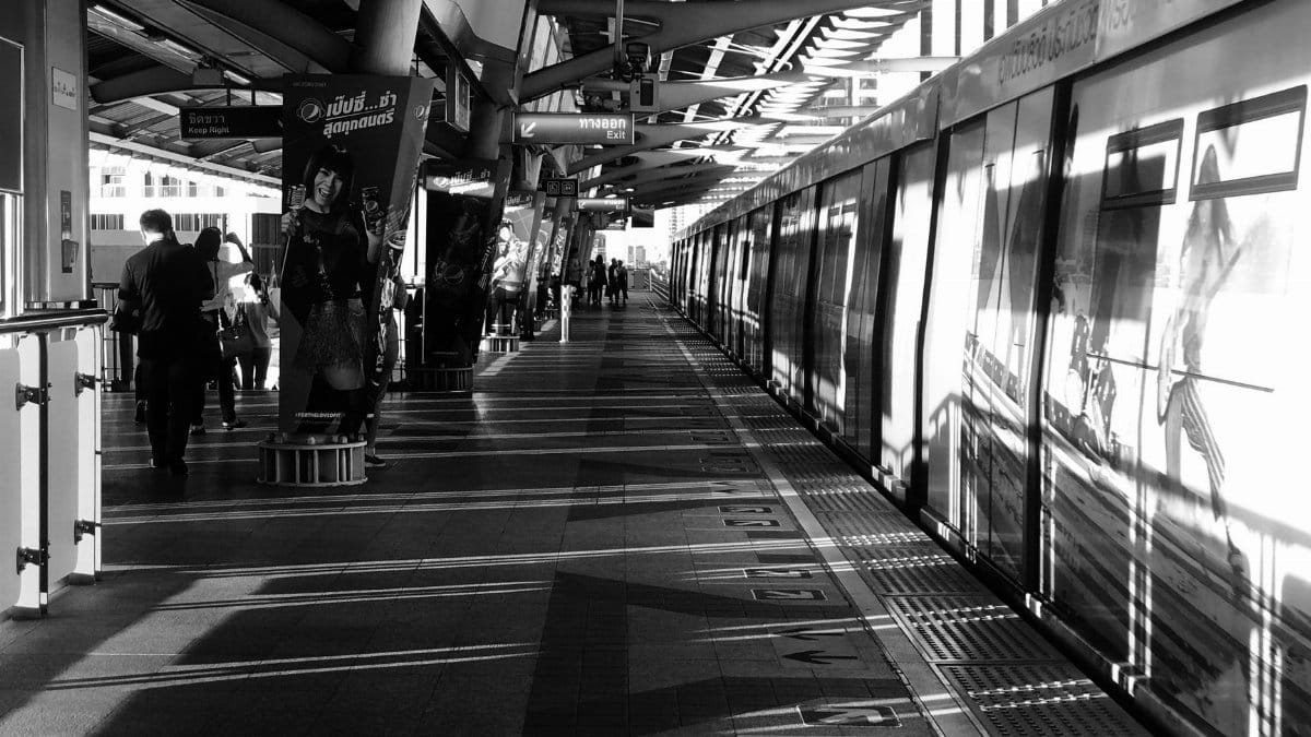 Black and white image capturing commuters at a railway platform in Khwaeng Samsen Nai, Bangkok, Thailand.