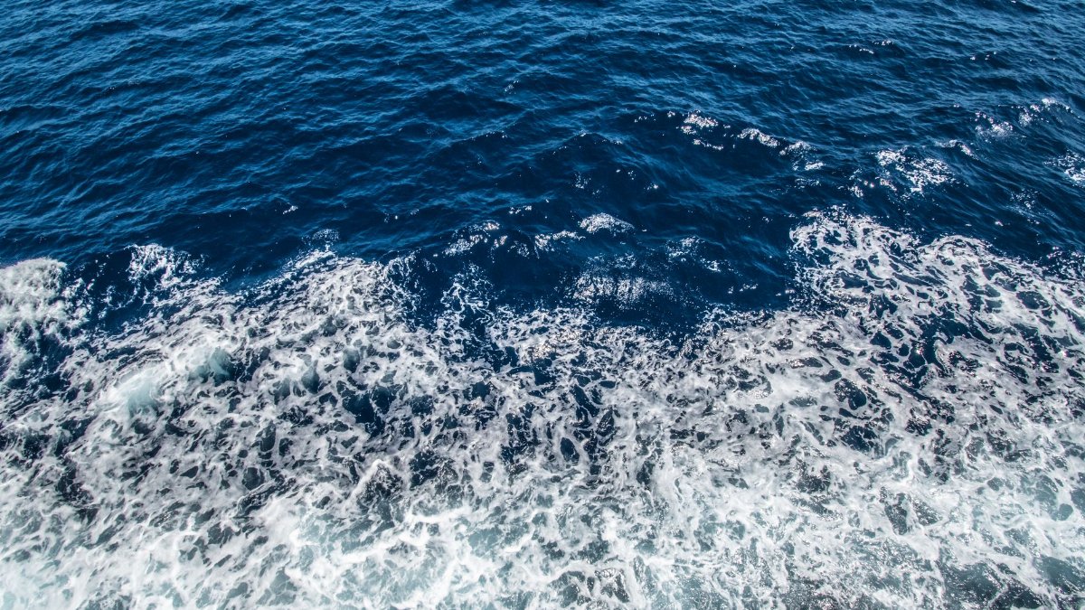 Aerial view of the ocean's dynamic waves and seafoam, showcasing its vibrant blue hues.