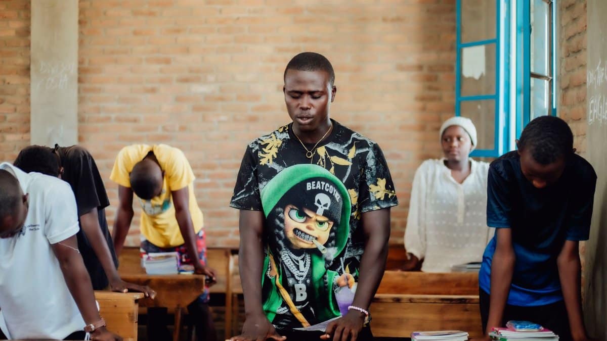 A group of African students in a classroom participating in a prayer session.