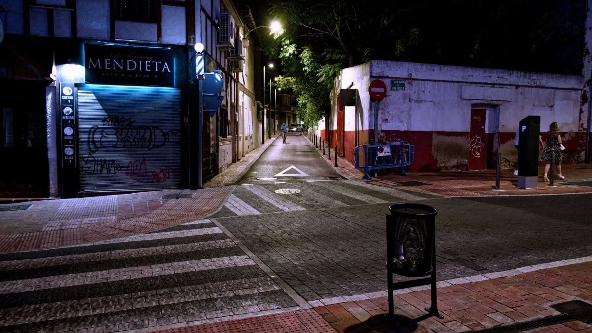 Quiet urban street scene at night with graffiti and closed storefronts.