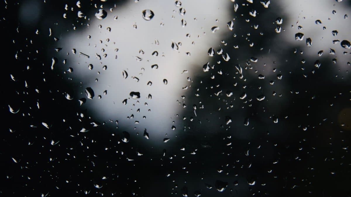 Close-up of rain droplets on a glass window with a dark, blurred background.
