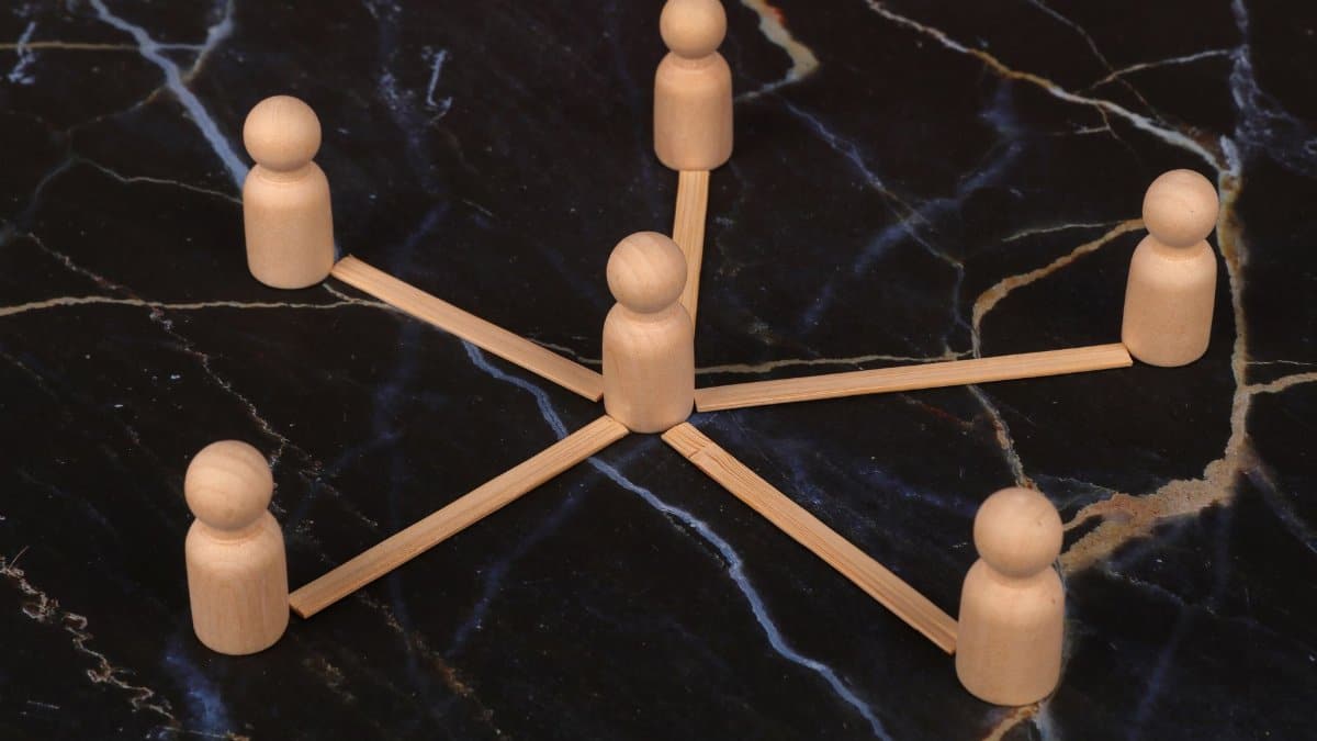 Wooden figures arranged in a network pattern on a marble surface, symbolizing connection or teamwork.