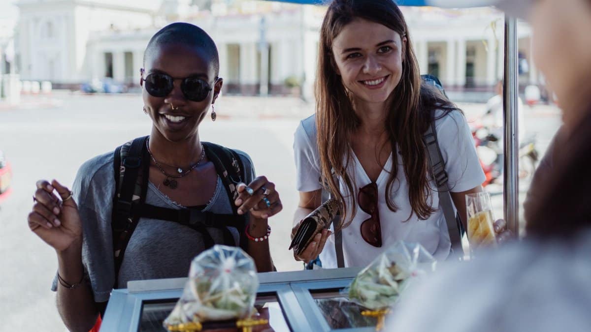 Two women enjoying street food at an outdoor market, exuding joy and travel spirit.