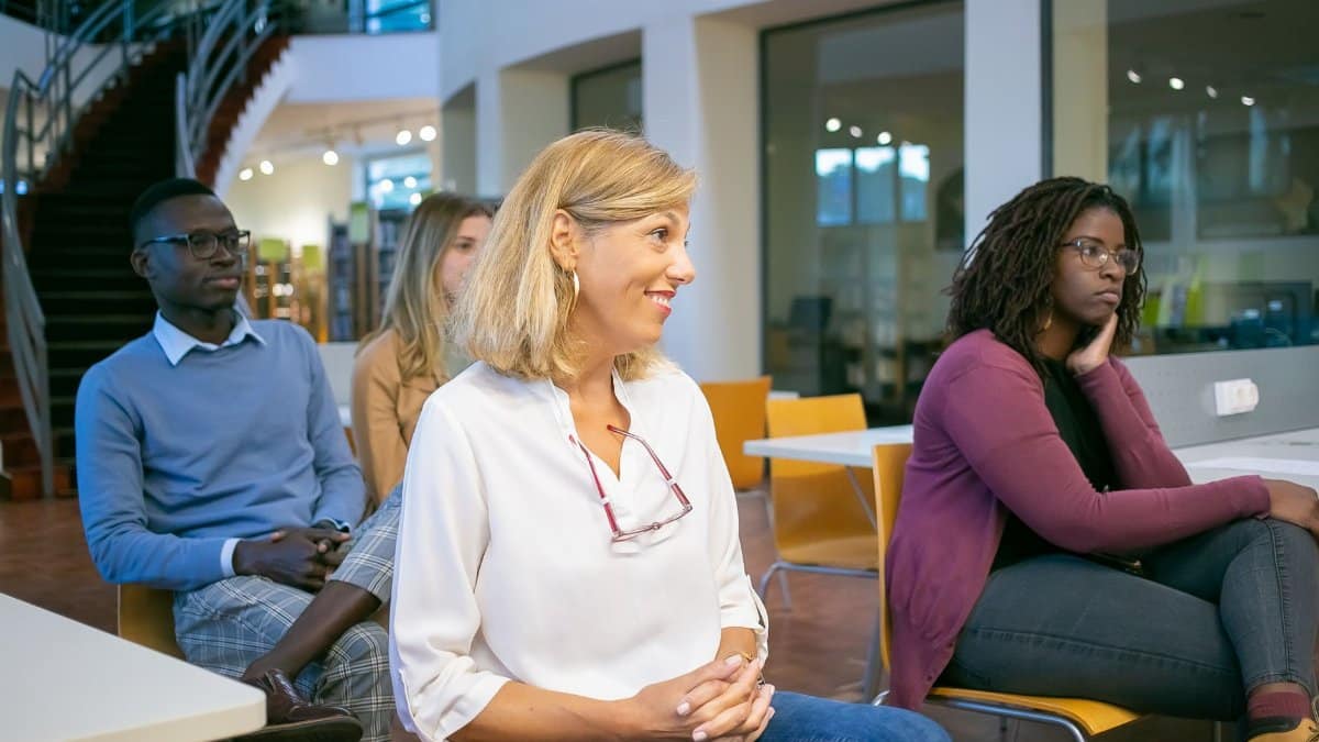 Multiethnic group of students with teacher sitting on chairs in classroom and attentively listening at presentation