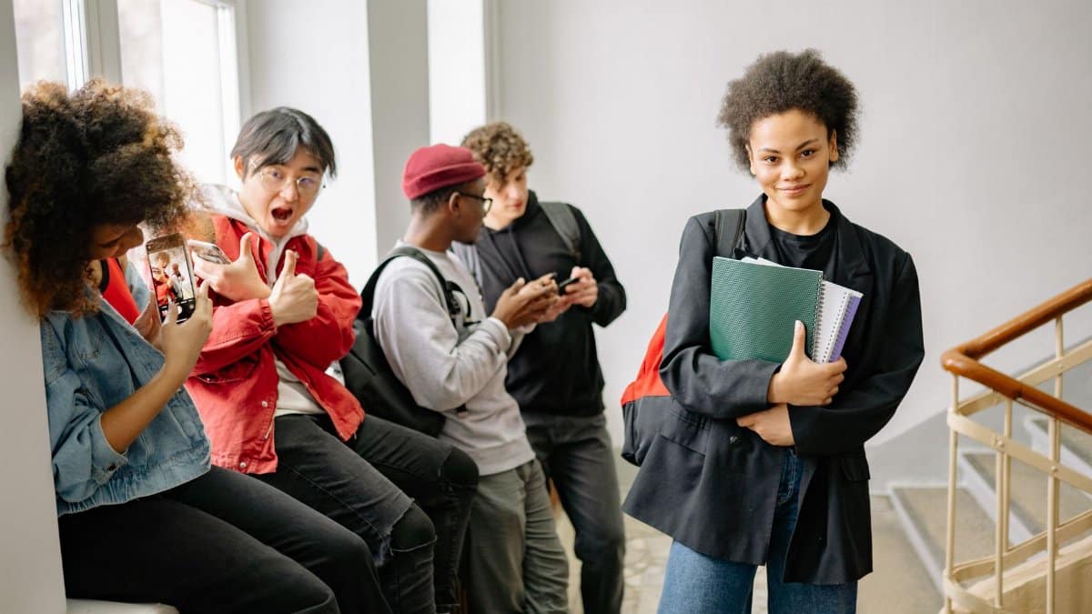 A group of diverse college students using smartphones and chatting in a hallway, representing modern student life.