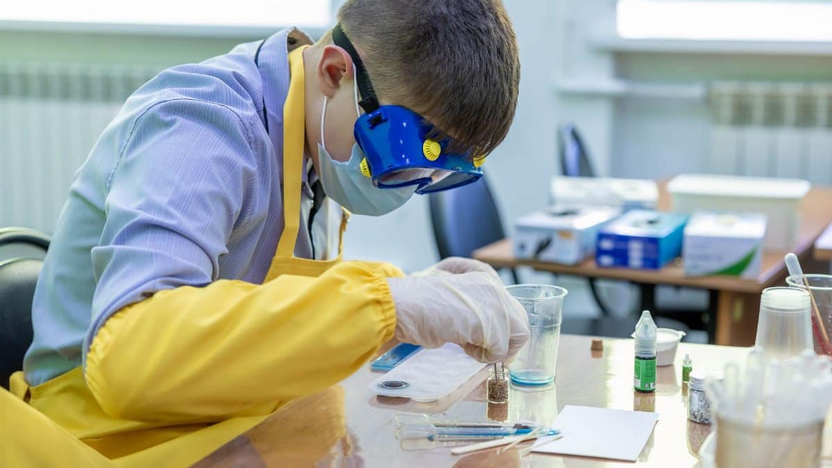 Young student in protective gear performing a chemistry experiment in a laboratory setting.